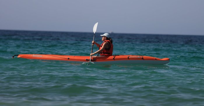 Woman kayaking in vibrant orange kayak on open ocean on a sunny summer day.