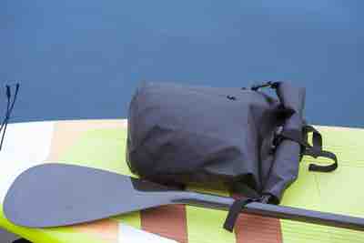 Close up of stylish waterproof bag lying on yellow stand up paddle board next to the paddle. Dry bag