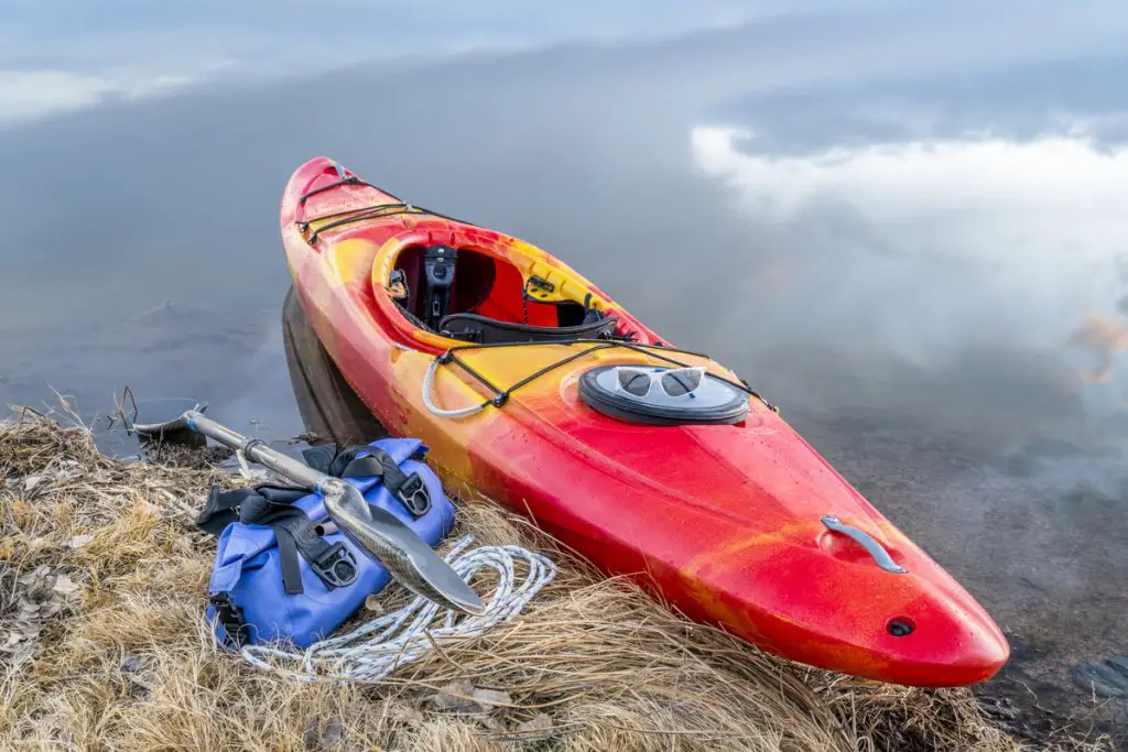 whitewater kayak on a lake shore with a paddle and waterproof duffel, early spring scenery in northern Colorado