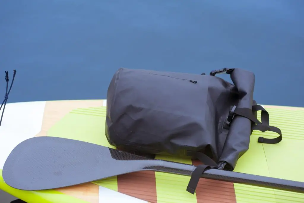 Close up of stylish waterproof bag lying on yellow stand up paddle board next to the paddle. Dry bag