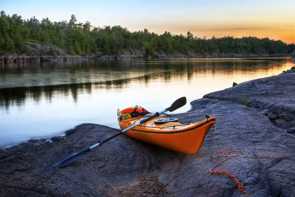 Orange kayak left on a rocky river bank with the sunset skies on the background