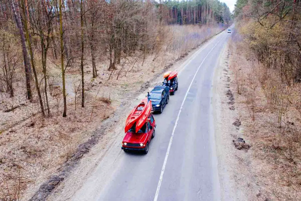 Several cars with kayaks on roof rack driving on the road among trees, beautiful sunny day. View from above