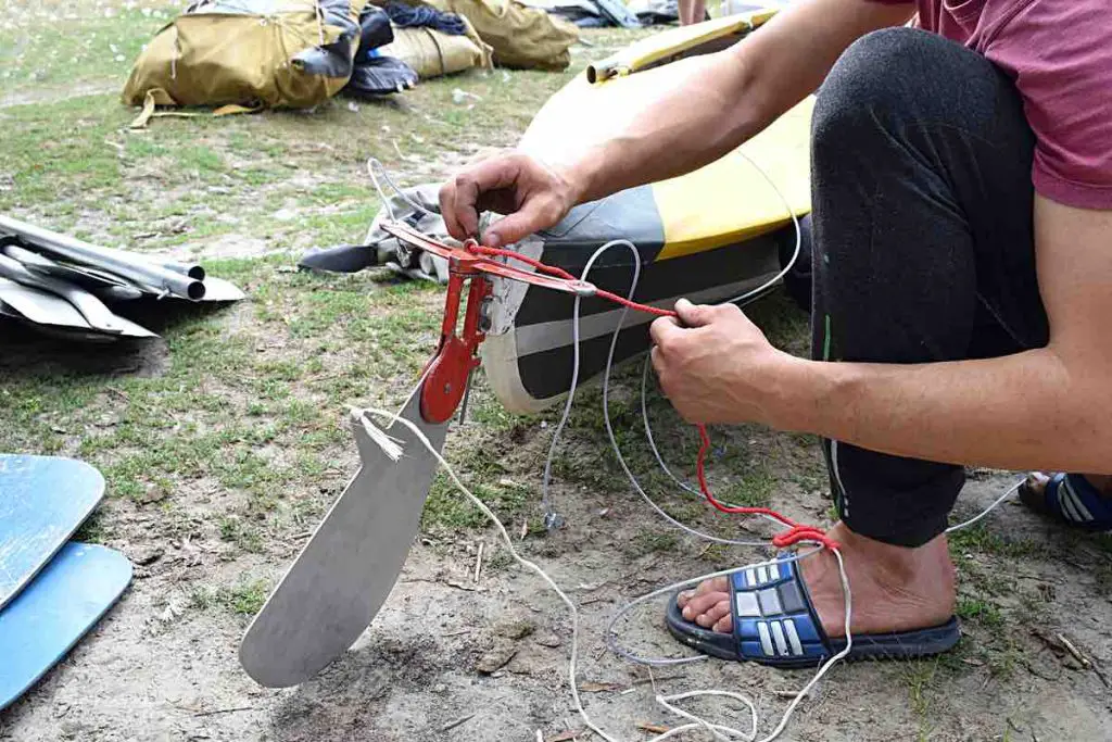 a man mounts a steering wheel on a kayak on the river bank before launching