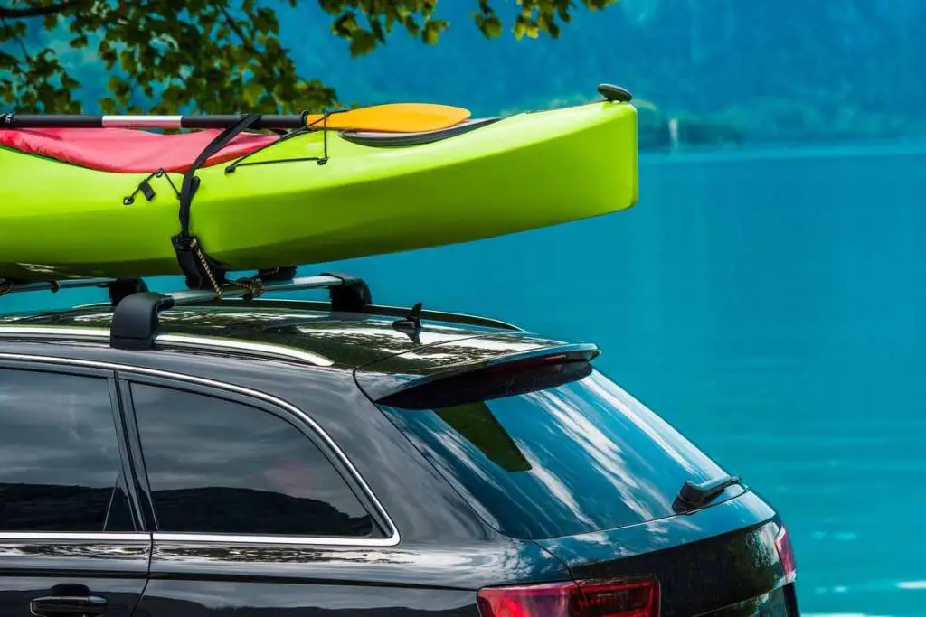 Kayak Roof Rack and the Green Kayak Mounted on the Vehicle Roof. Vacation on the Water Theme. Scenic Lake in the Background.