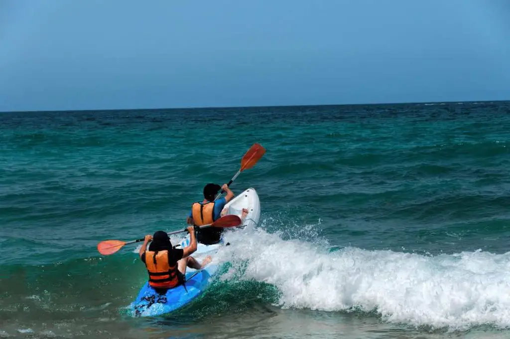 Two athletes compete in the kayak with sea waves trying to swim away from the shore