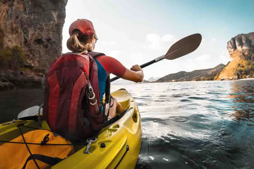 Lady paddling the kayak in the calm bay with limestone mountains