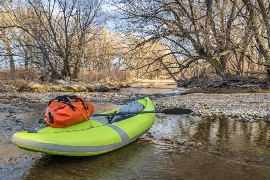 whitewater inflatable kayak with a paddle and waterproof duffel on a river  shore - Poudre River in Fort Collins, Colorado in early spring scenery and low water, water sports and recreation concept