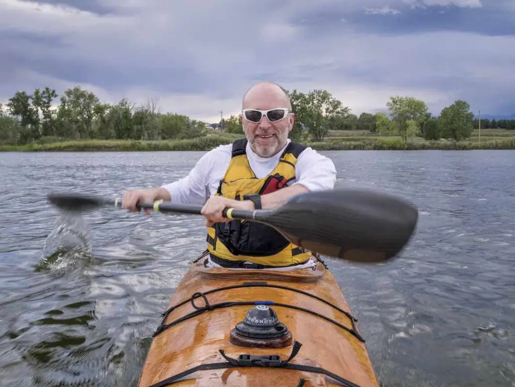 a bow view of a senior male paddling a home-built wooden sea kayak on a lake in Colorado, focus on face with arms and paddle in a motion blur