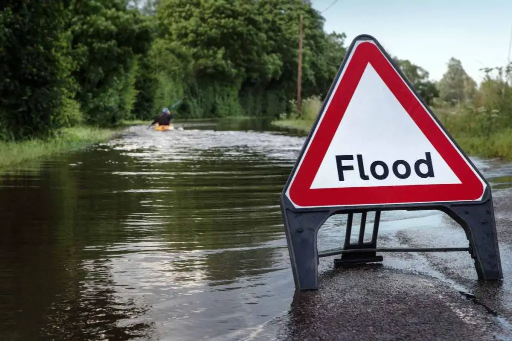 county road in essex of flooded road with a person paddling  down the road in a kayak