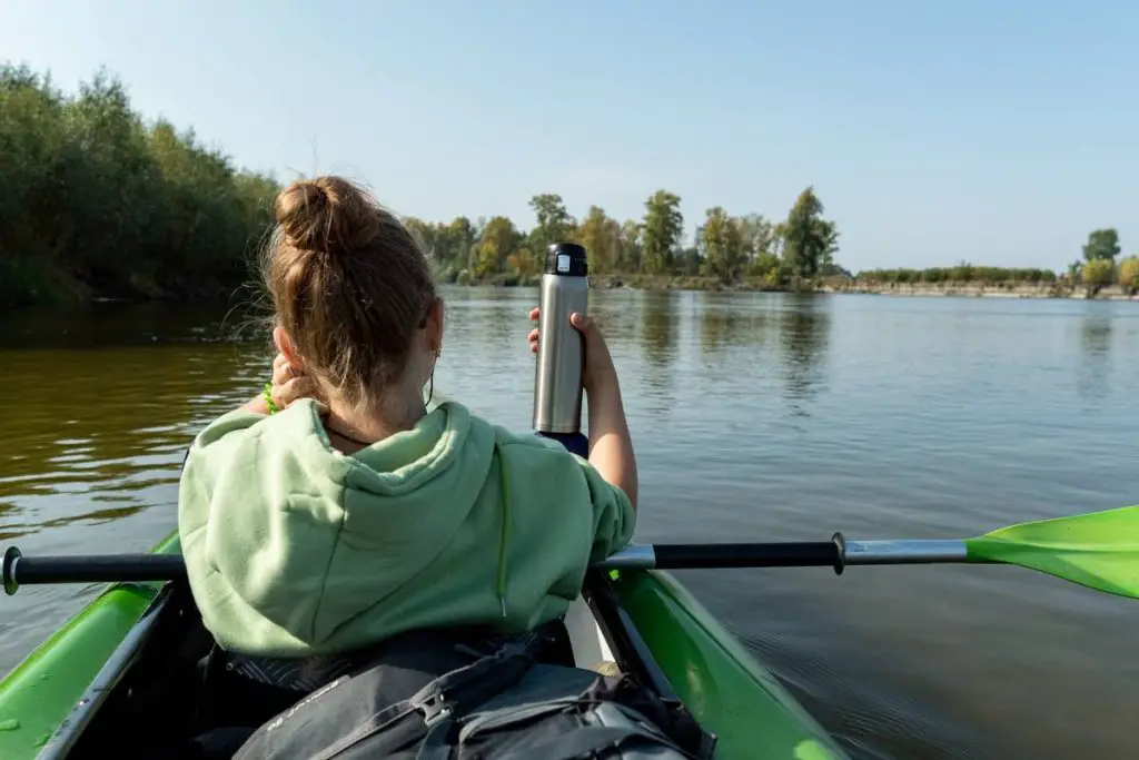 The girl in the boat holds a thermos for tea. Rafting down the river with a thermos. The girl is rafting.