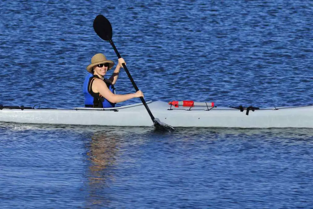 Cute young woman in straw hat is kayaking in idyllic blue waters of Mission Bay, San Diego, California