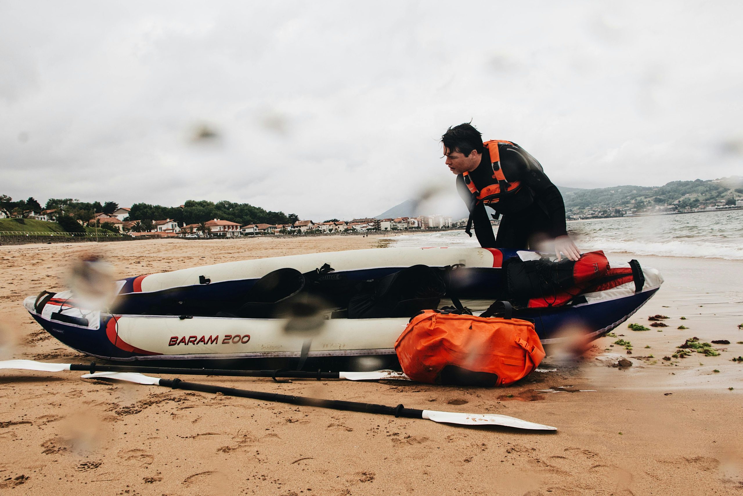 A man in a wetsuit preparing a kayak on a sandy shore, readying for a watersport adventure.