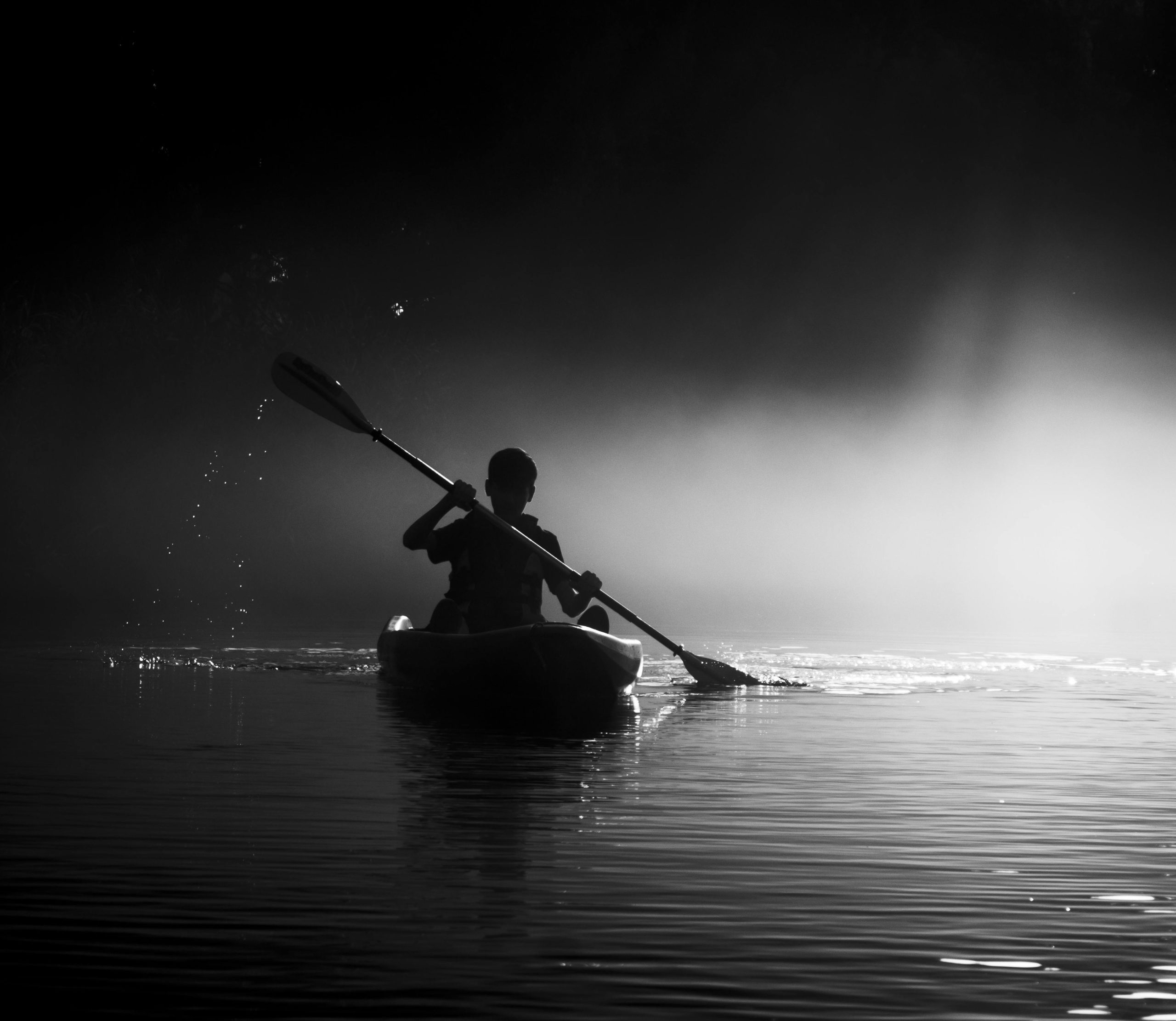 A striking monochrome image of a kayaker paddling through mist at dawn.