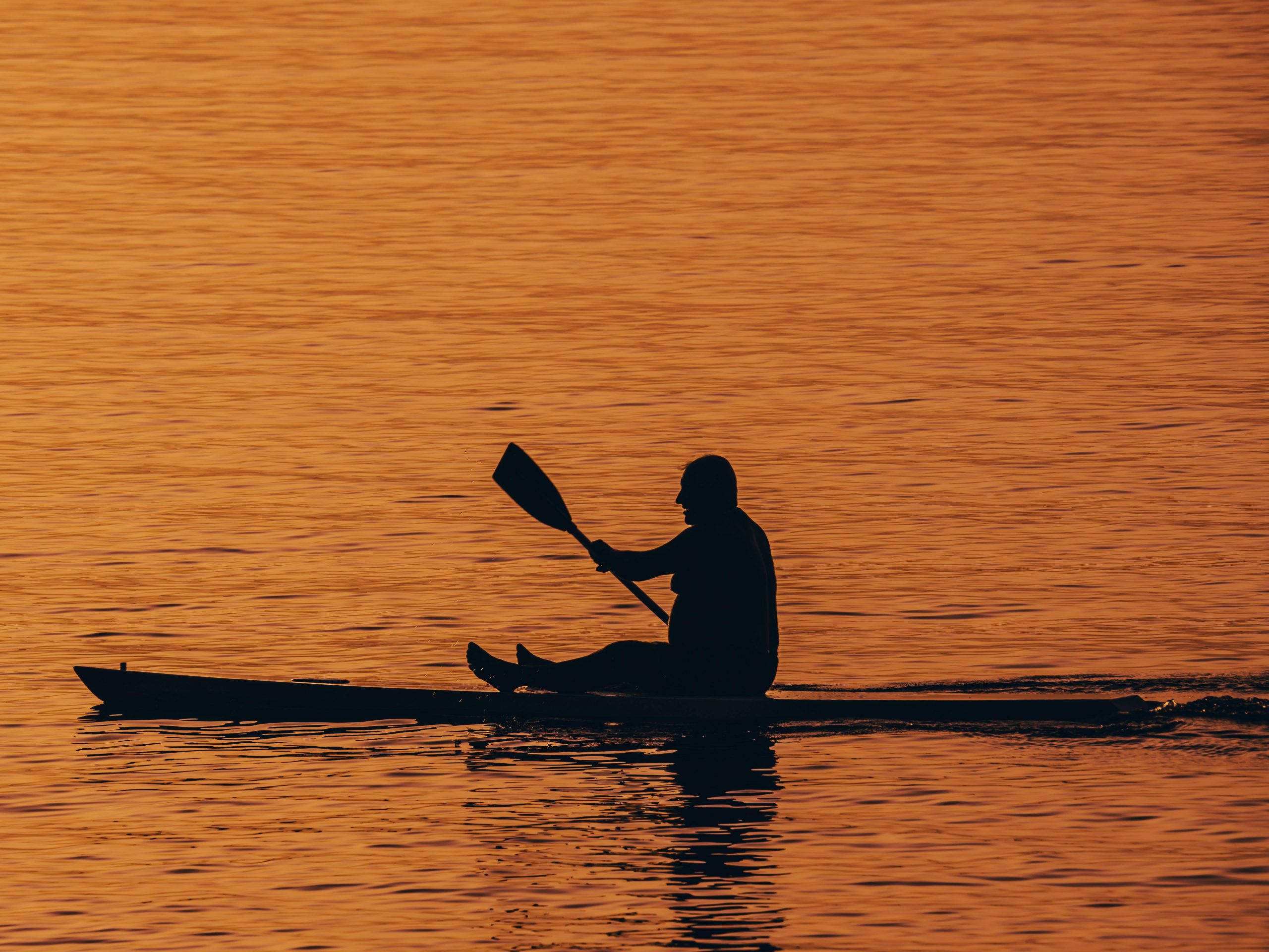 A silhouette of a man kayaking during a stunning sunset, creating a peaceful and serene scene on the water.