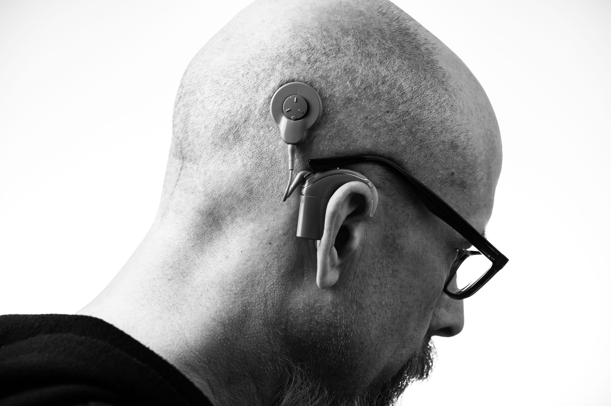 Black and white profile of a man wearing glasses and a hearing aid, studio shot.