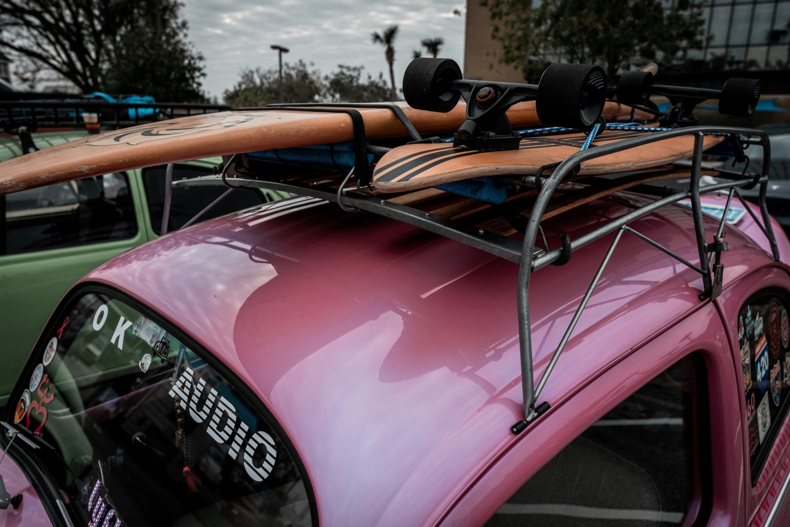 A vintage pink Volkswagen Beetle with a skateboard on the roof, parked outdoors.
