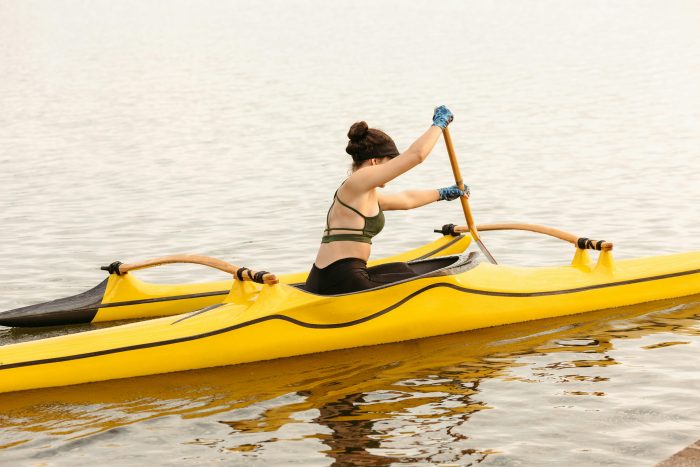 A young woman paddles a yellow kayak on a peaceful lake during a bright summer day.
