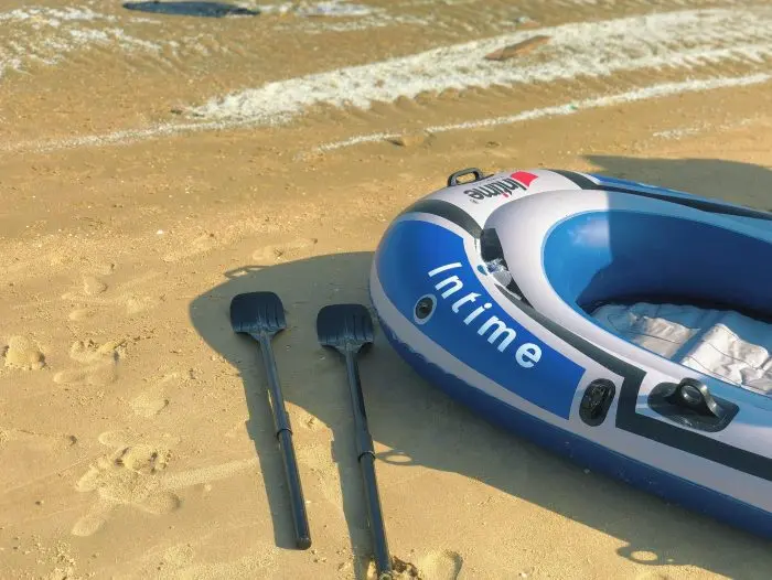 Close-up of an inflatable boat and oars on a sunny sandy beach, ideal for summer adventures.