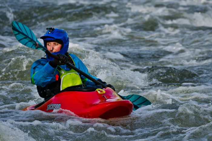 Female kayaker navigating through river rapids in an exciting adventure sport setting.