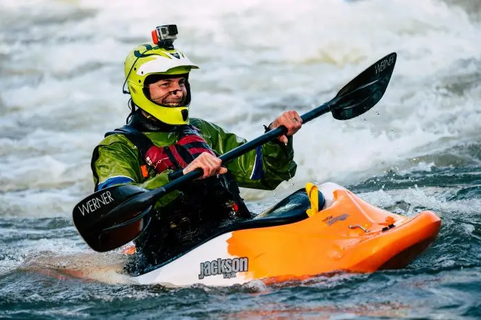An adventurous kayaker smiles while paddling through wild whitewater rapids.