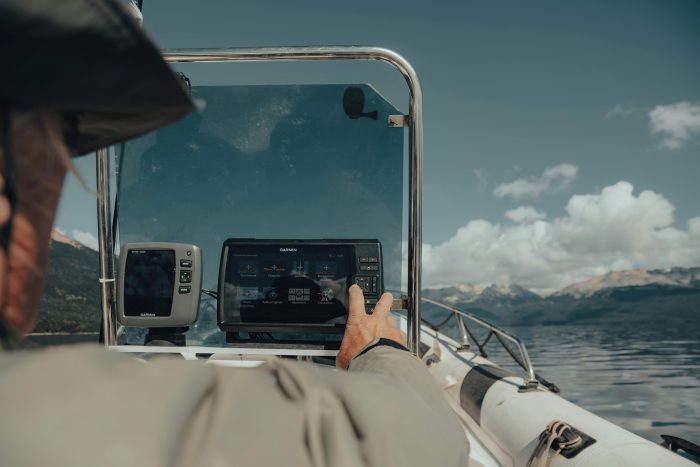 Man enjoying a sunny day while navigating a motorboat using GPS technology on a clear river.