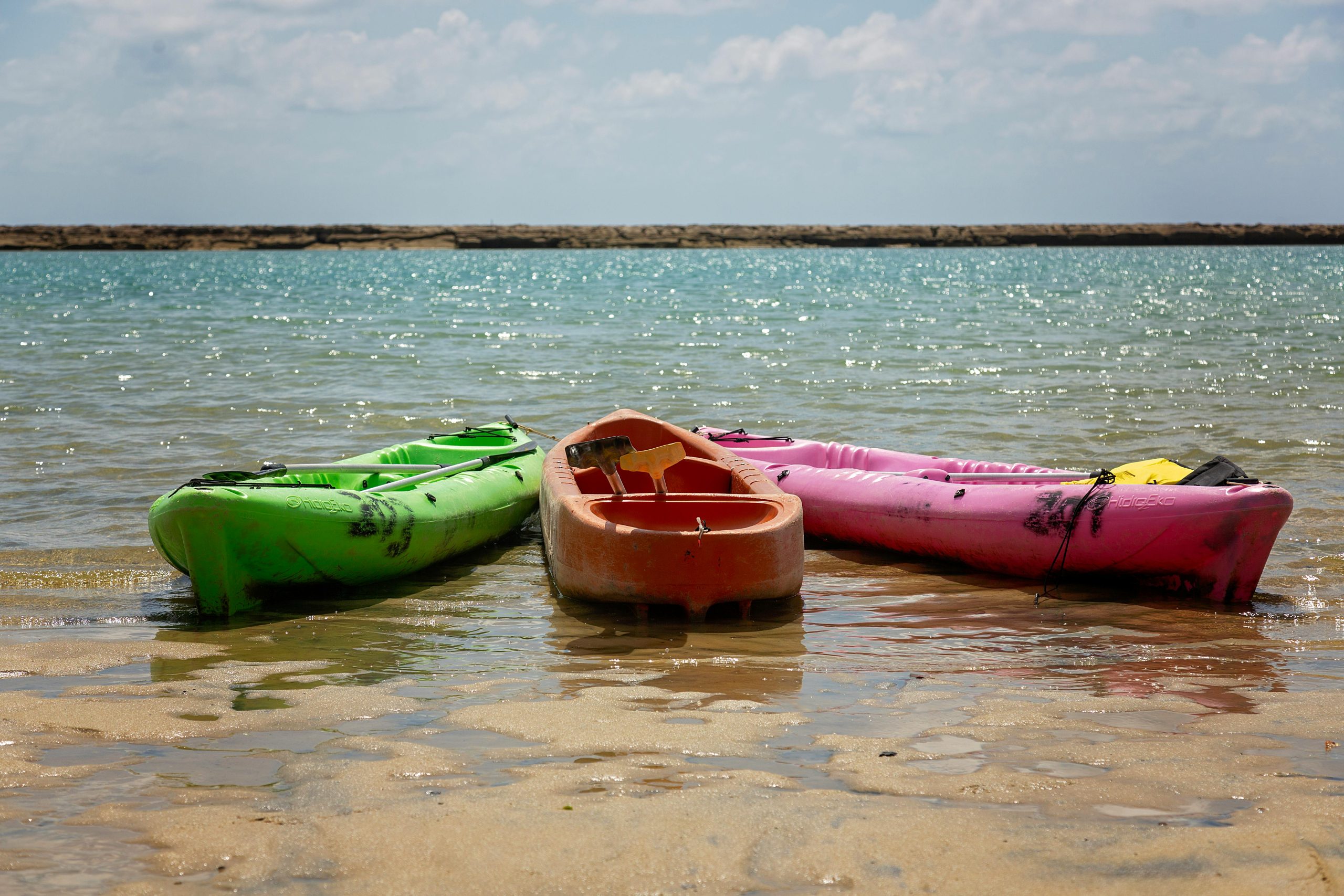 Three vibrant kayaks rest on a sunlit beach, inviting a day of adventure.