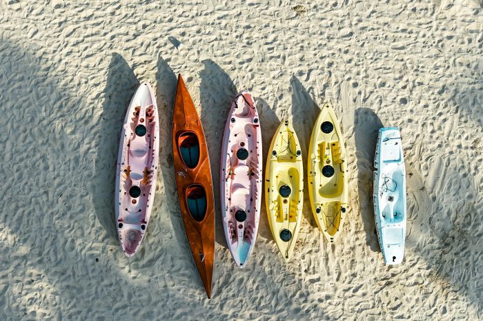 Aerial view of vibrant kayaks resting on sunlit sandy beach, perfect for outdoor adventure imagery.