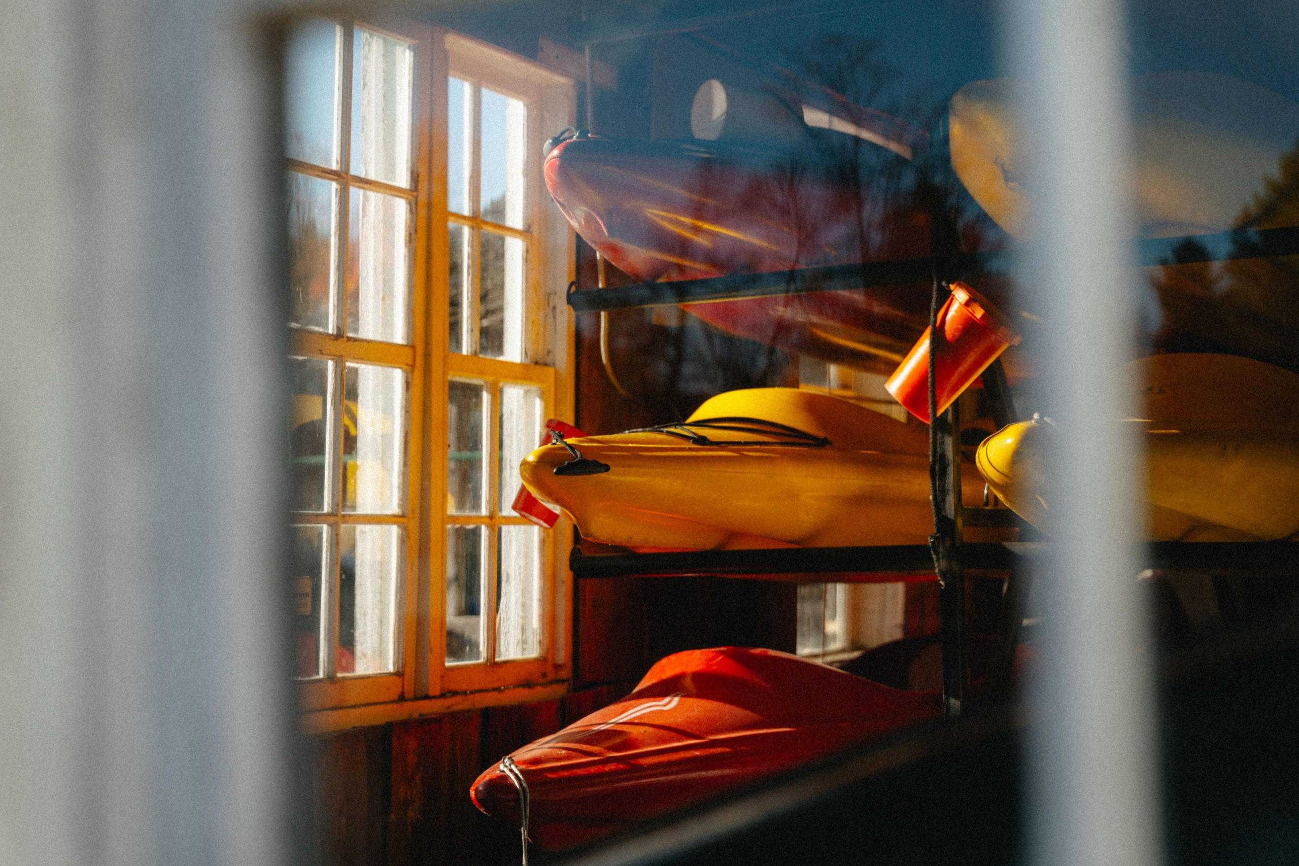 Colorful kayaks stored indoors bask in warm sunlight through a window in North Hatley, Québec.
