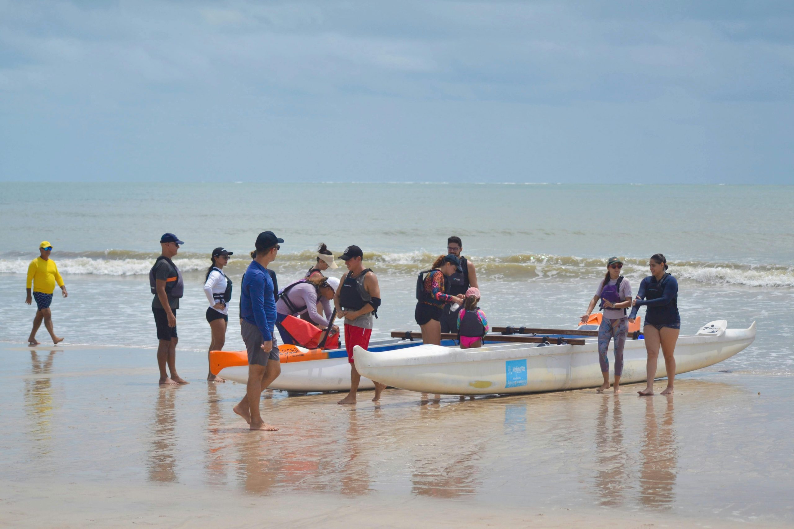 People gathering on the shore readying kayaks for a coastal adventure on a sunny day.