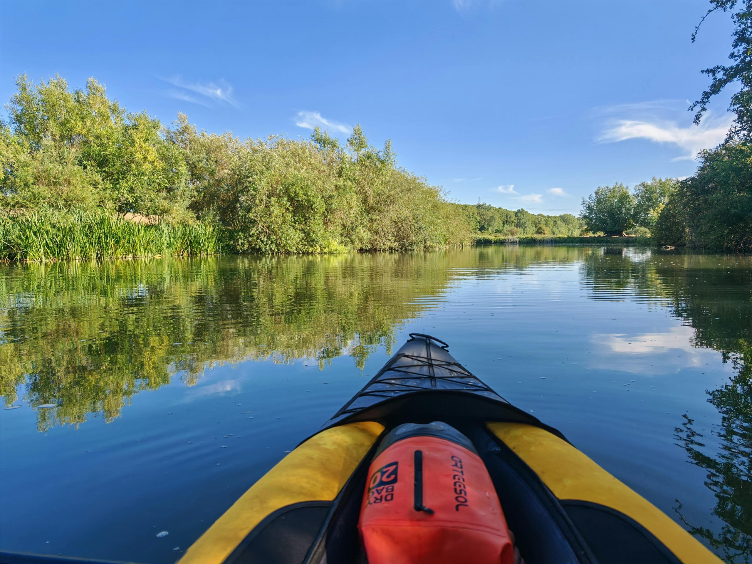 Experience the tranquility of kayaking on a calm river surrounded by lush greenery under a clear blue sky.
