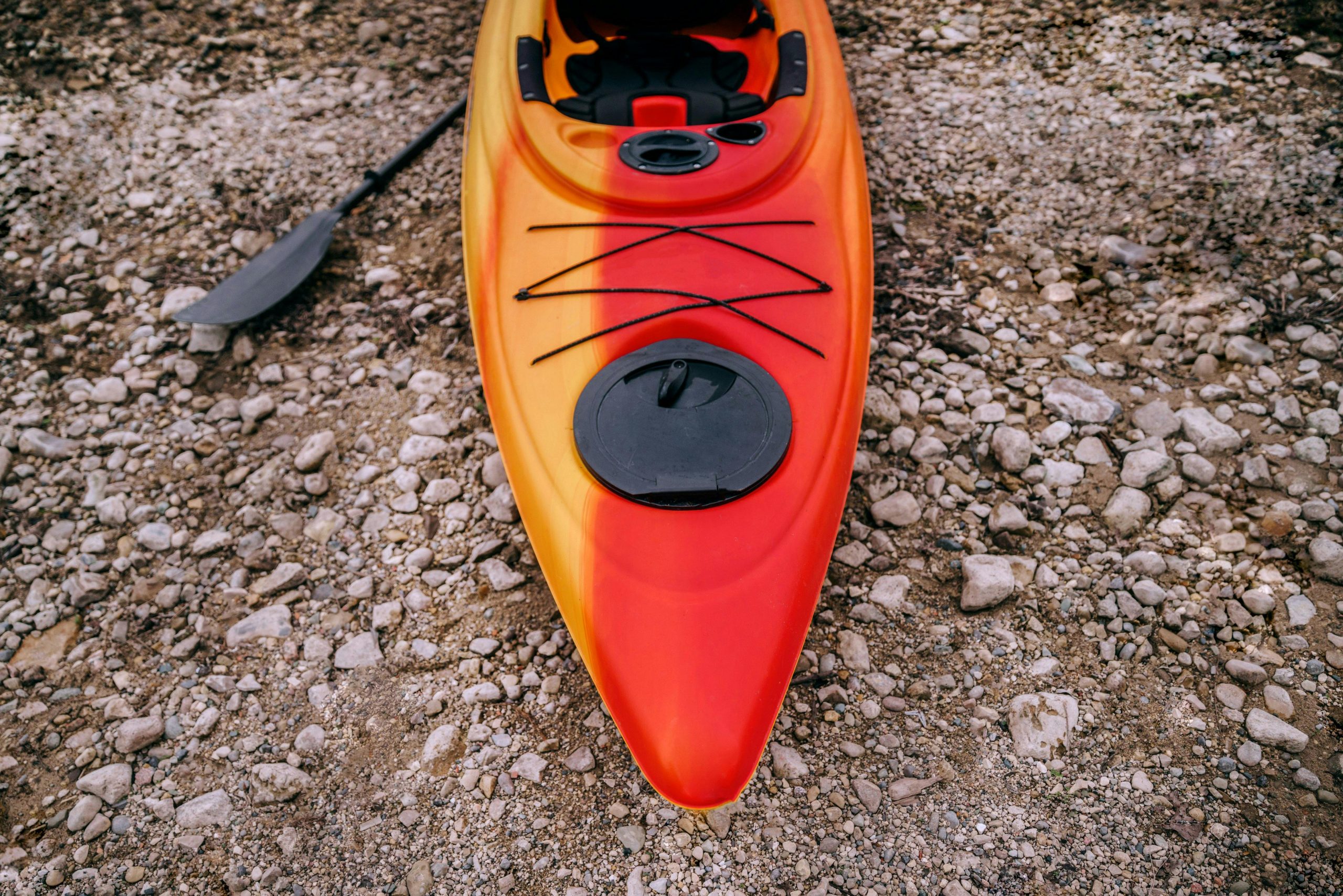 A vibrant red kayak rests on a rocky shoreline, ideal for outdoor adventures.
