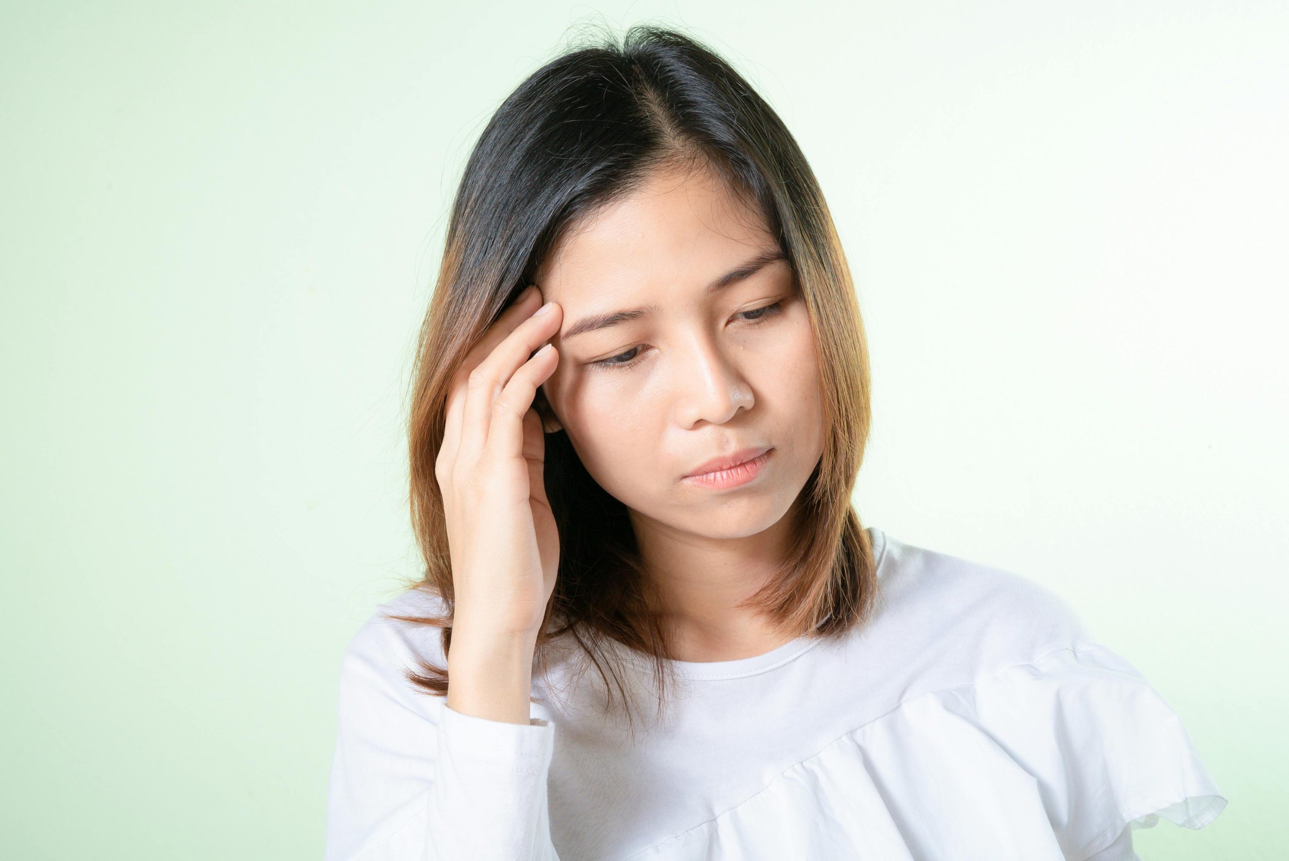 Contemplative young woman in a white top, deep in thought against a light background.