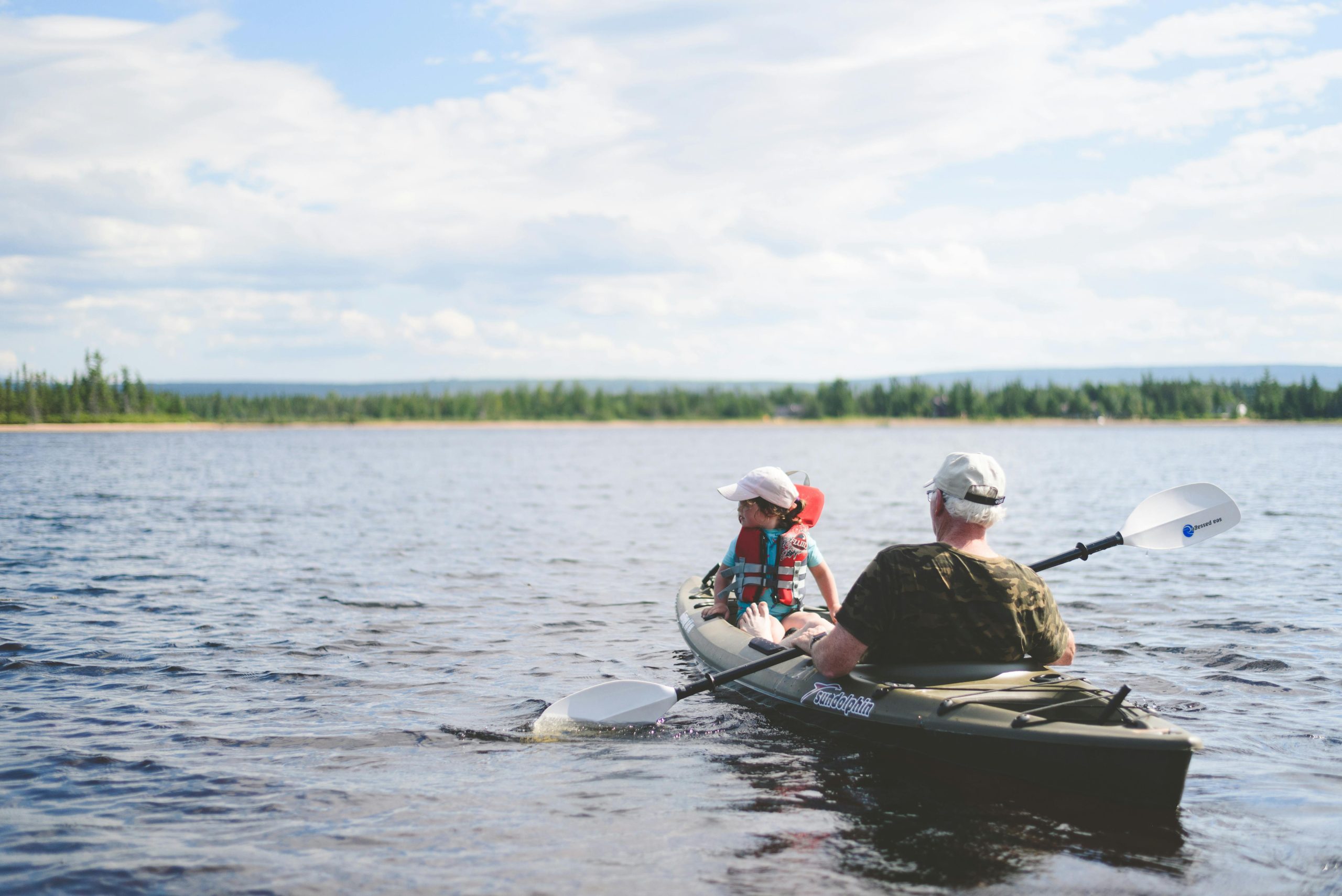 A grandfather and grandson kayaking together on a serene lake under a blue sky, enjoying outdoor adventure.