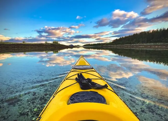 Serene kayaking scene with yellow kayak on clear Norwegian river under summer sky.