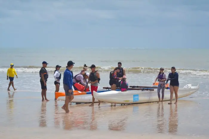 People gathering on the shore readying kayaks for a coastal adventure on a sunny day.