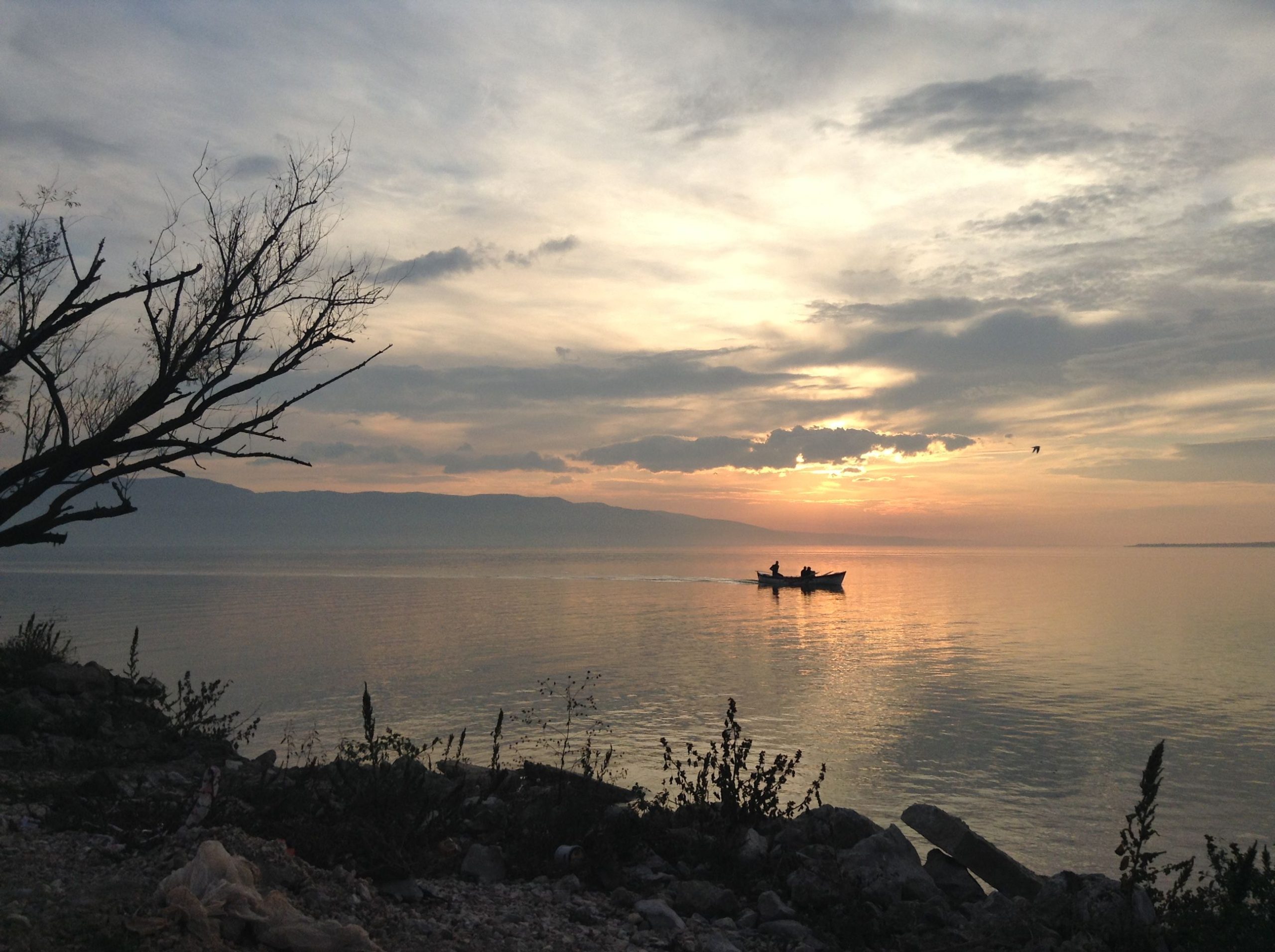 A boat glides through calm waters at sunrise in Bursa, Turkey, with a dramatic silhouette and vibrant cloudscape.