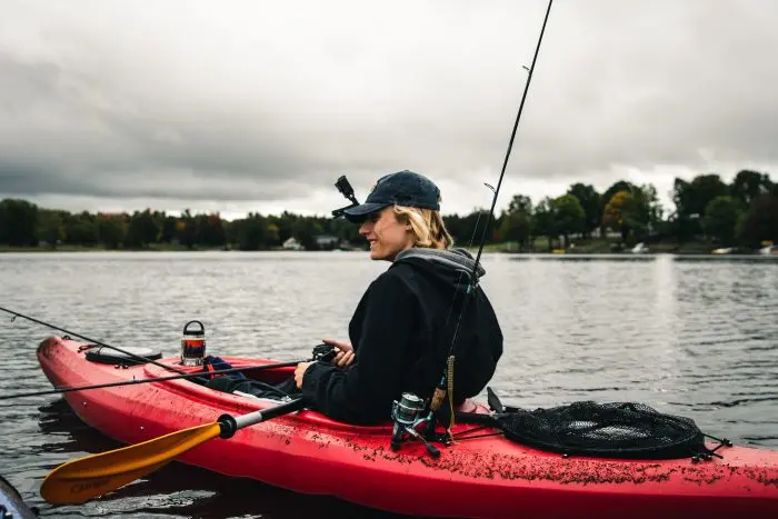 Person fishing from a kayak on a serene lake under overcast skies.
